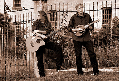 guitar player and mandolin player in from of gothic fence
