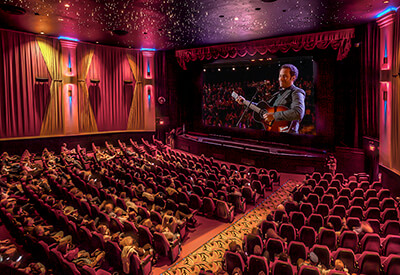 wide interior shot of movie theater with guitar player on screen
