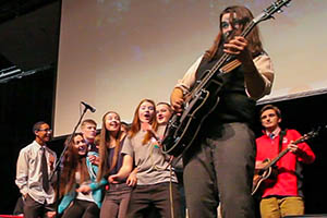 Musician Seth Bernard playing guitar on stage with high school students watching